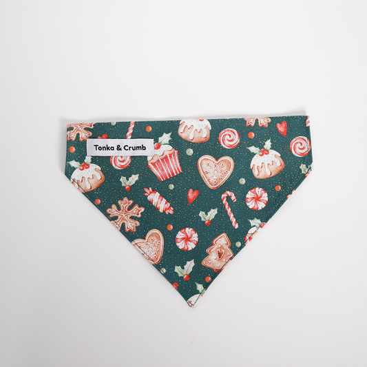 Christmas-themed dog bandana with candy cane, gingerbread, and cake designs on a green background.